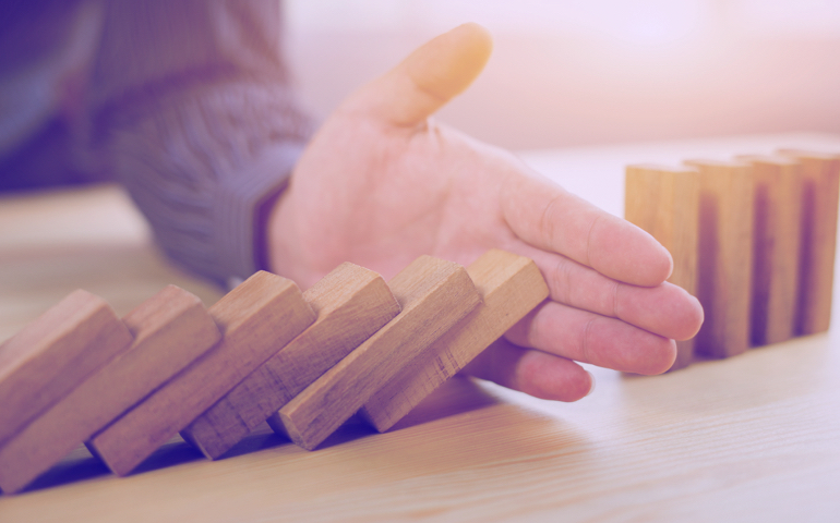 Wooden dominoes falling, human hand stopping it.