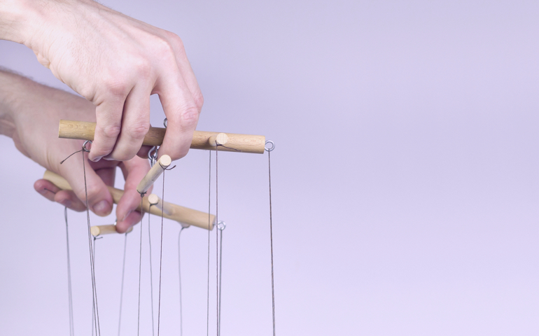 Hand holding the strings of a puppet.